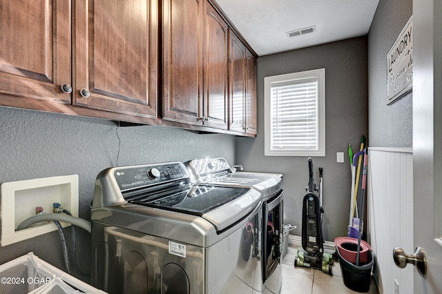 clothes washing area featuring cabinets, light tile patterned floors, and washing machine and clothes dryer