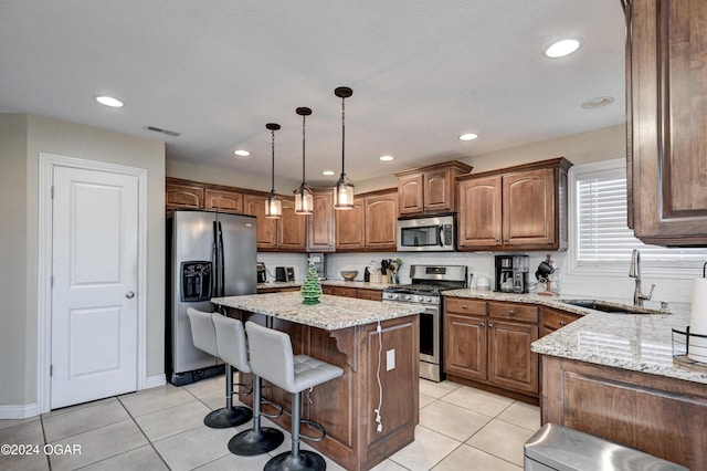 kitchen featuring sink, a center island, light stone counters, pendant lighting, and appliances with stainless steel finishes