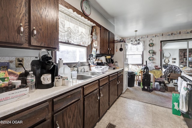 kitchen featuring dark brown cabinetry, sink, a notable chandelier, white fridge, and pendant lighting