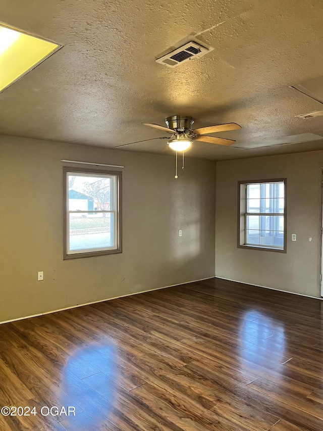 empty room with a textured ceiling, dark hardwood / wood-style floors, plenty of natural light, and ceiling fan