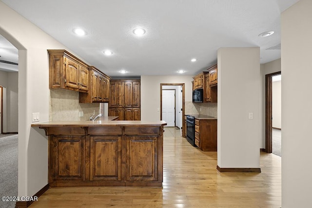 kitchen with backsplash, kitchen peninsula, light hardwood / wood-style flooring, and black appliances