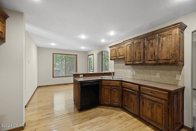 kitchen with kitchen peninsula, light wood-type flooring, backsplash, sink, and black dishwasher