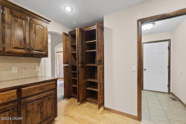 interior space featuring backsplash, dark brown cabinets, a textured ceiling, and light wood-type flooring