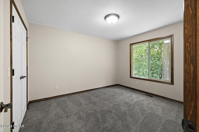 unfurnished bedroom featuring a textured ceiling and dark carpet