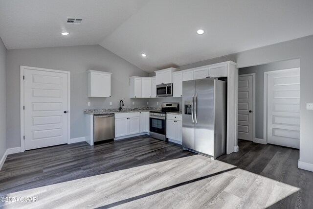 kitchen with appliances with stainless steel finishes, vaulted ceiling, dark wood-type flooring, sink, and white cabinets