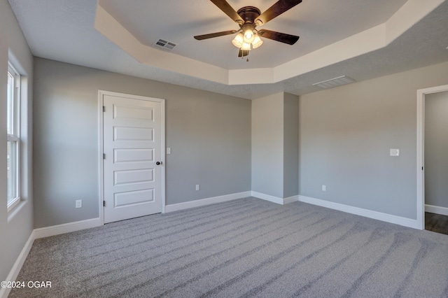 carpeted empty room featuring ceiling fan, a healthy amount of sunlight, and a tray ceiling