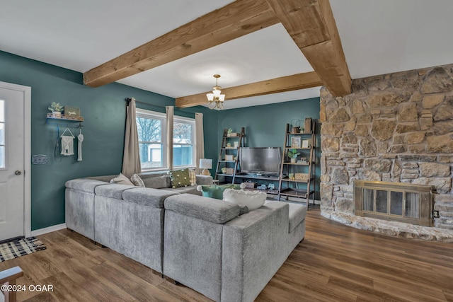 living room featuring beamed ceiling, a stone fireplace, wood-type flooring, and an inviting chandelier