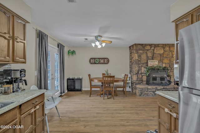 kitchen with stainless steel refrigerator, light stone countertops, light hardwood / wood-style flooring, and a wood stove