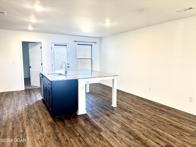 kitchen with a kitchen island with sink, sink, dark hardwood / wood-style floors, light stone counters, and a kitchen bar