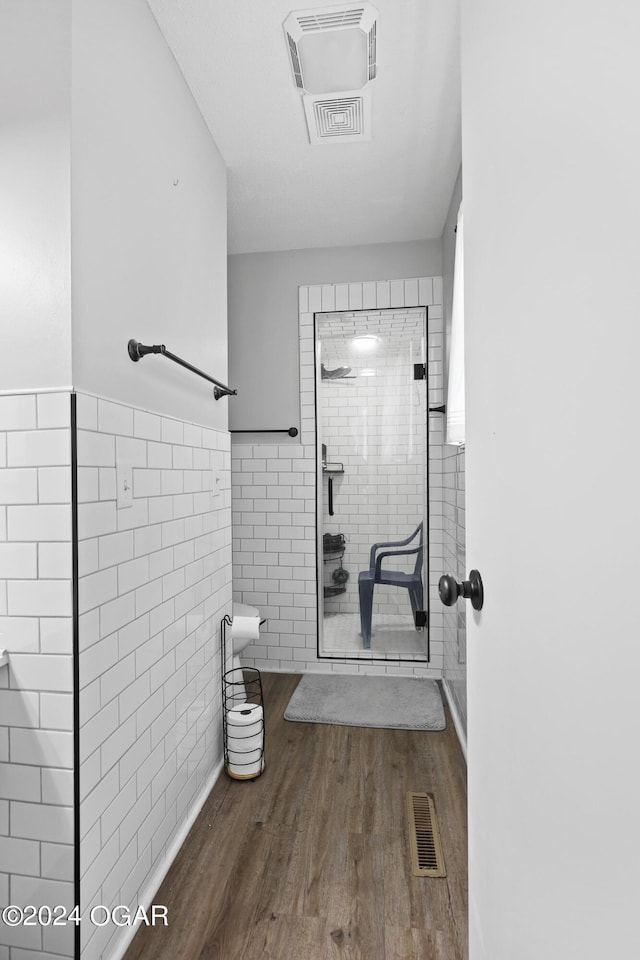 bathroom with hardwood / wood-style floors, tiled shower, and tile walls