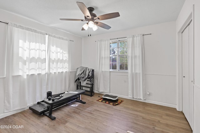 exercise area with ceiling fan, light hardwood / wood-style flooring, and a textured ceiling