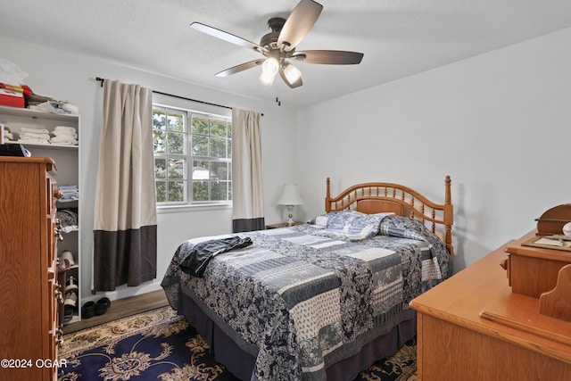 bedroom with a textured ceiling, ceiling fan, and dark wood-type flooring