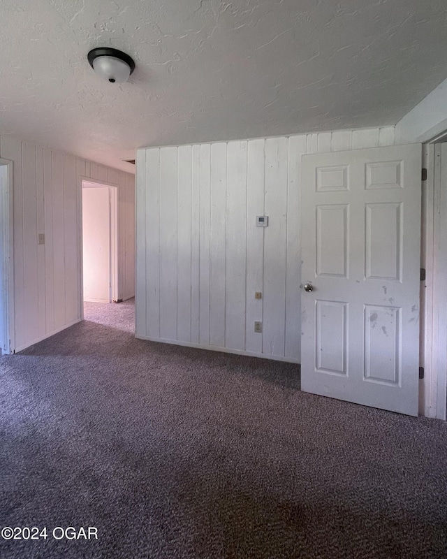 carpeted empty room featuring wood walls and a textured ceiling