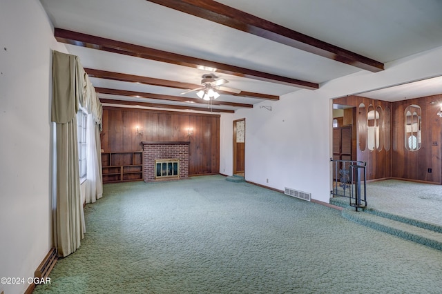 unfurnished living room featuring carpet, a brick fireplace, ceiling fan, and wooden walls