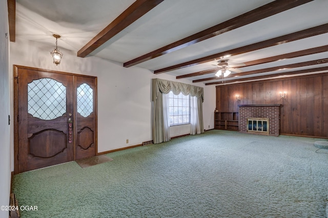 foyer entrance with carpet, wood walls, ceiling fan, a fireplace, and beam ceiling