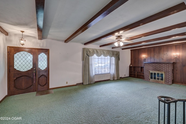 carpeted entrance foyer featuring ceiling fan, wooden walls, beamed ceiling, and a brick fireplace