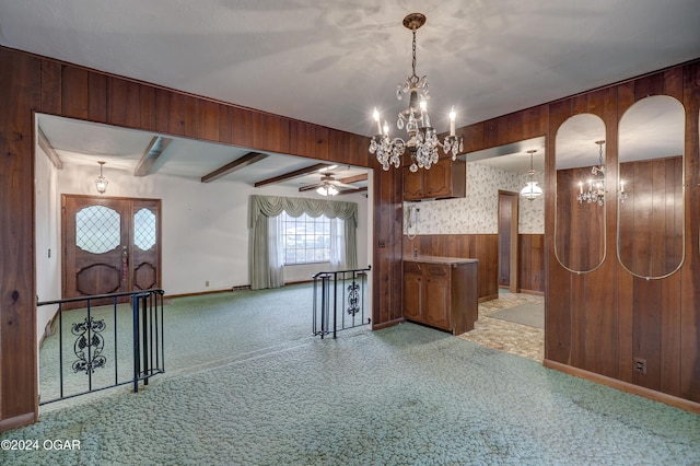 interior space featuring ceiling fan with notable chandelier, wood walls, light colored carpet, and hanging light fixtures