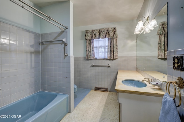 full bathroom featuring toilet, vanity, tiled shower / bath combo, and tile walls