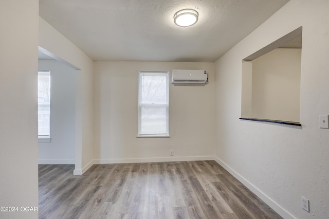 unfurnished room featuring a textured ceiling, light hardwood / wood-style floors, a wall unit AC, and plenty of natural light