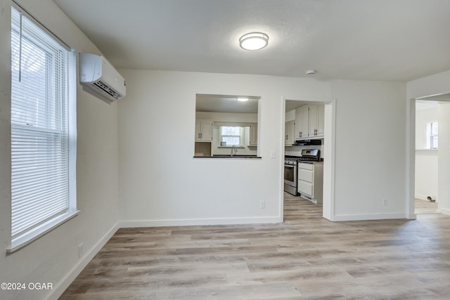 unfurnished dining area with a textured ceiling, light wood-type flooring, a wall unit AC, and a wealth of natural light