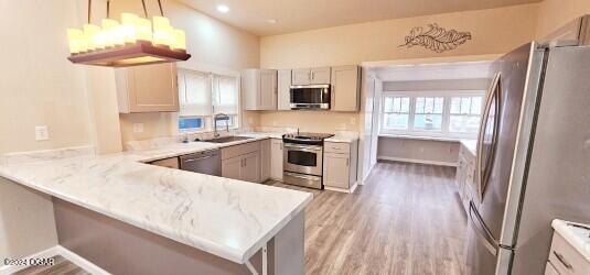 kitchen with kitchen peninsula, light wood-type flooring, stainless steel appliances, sink, and pendant lighting