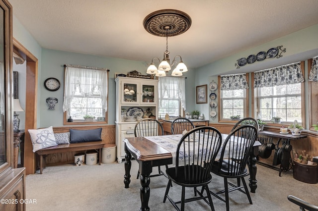 carpeted dining area with a healthy amount of sunlight, a textured ceiling, and a notable chandelier