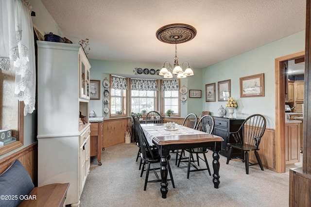 carpeted dining area with wooden walls, a chandelier, and a textured ceiling