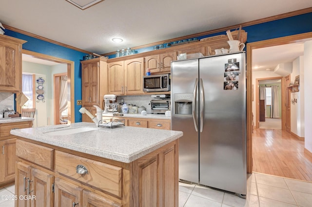 kitchen with light tile patterned flooring, sink, crown molding, appliances with stainless steel finishes, and a kitchen island