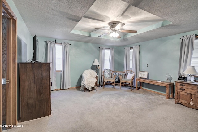 sitting room with light carpet, a textured ceiling, a tray ceiling, and ceiling fan