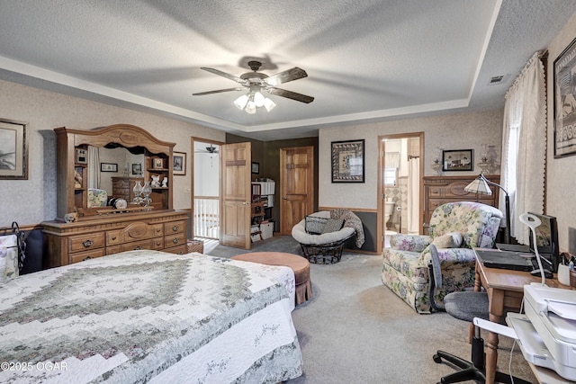 carpeted bedroom featuring a raised ceiling, a textured ceiling, ensuite bath, and ceiling fan