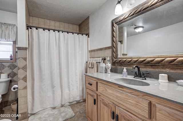 bathroom with vanity, a textured ceiling, toilet, and tile walls