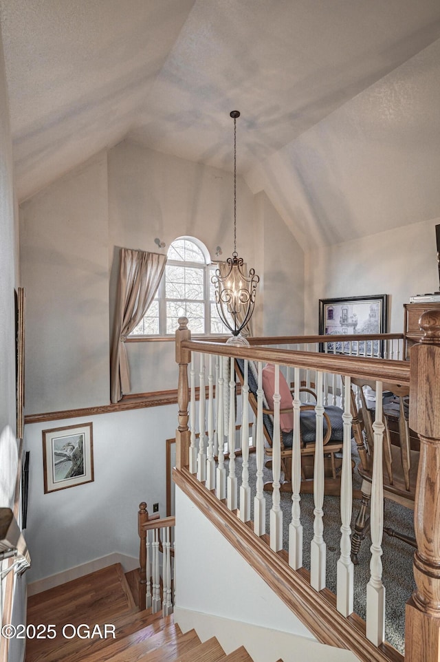 staircase with a chandelier, vaulted ceiling, and hardwood / wood-style flooring