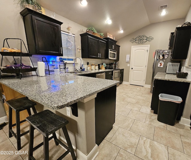 kitchen featuring lofted ceiling, sink, light stone countertops, appliances with stainless steel finishes, and a breakfast bar area