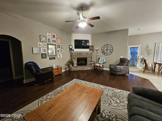 living room with ceiling fan, wood-type flooring, and a brick fireplace