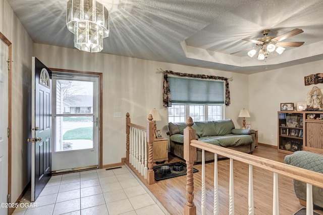 interior space featuring light tile patterned floors, ceiling fan with notable chandelier, a tray ceiling, and a wealth of natural light