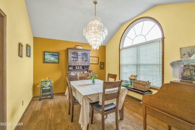 dining space with a notable chandelier, vaulted ceiling, and light wood-type flooring