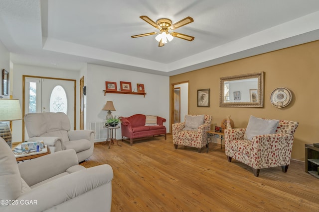 living room with french doors, light hardwood / wood-style floors, a raised ceiling, and ceiling fan