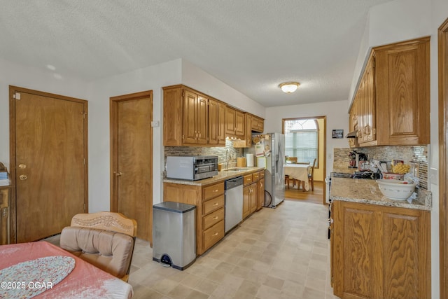 kitchen with light stone countertops, appliances with stainless steel finishes, a textured ceiling, and tasteful backsplash