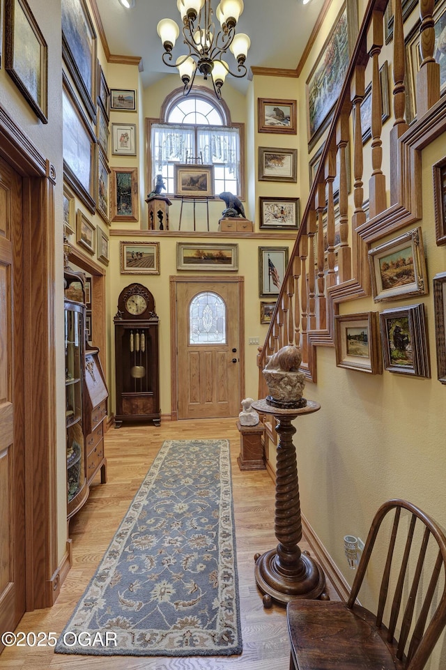 entryway featuring a chandelier, a high ceiling, light wood-type flooring, and crown molding