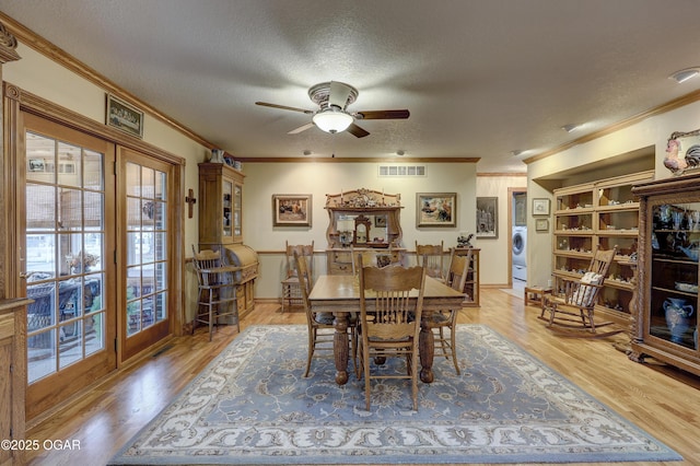 dining room featuring crown molding, light wood-type flooring, a textured ceiling, and washer / dryer