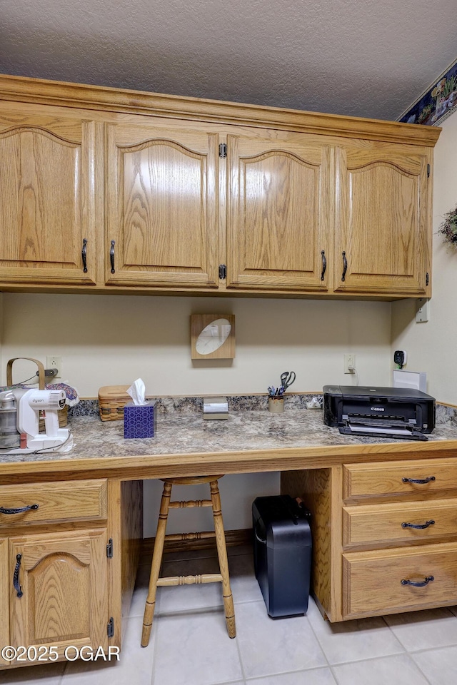 kitchen with light brown cabinets, built in desk, light tile patterned floors, and a textured ceiling