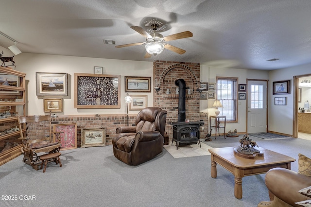 living room with a wood stove, ceiling fan, light colored carpet, and a textured ceiling