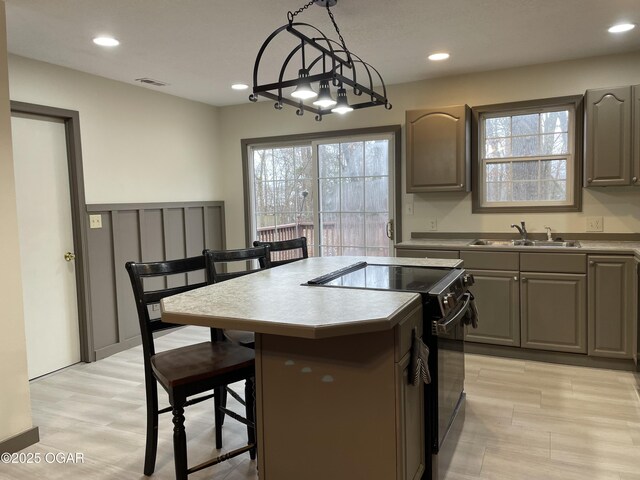 kitchen with black range with electric stovetop, sink, a kitchen breakfast bar, pendant lighting, and a kitchen island