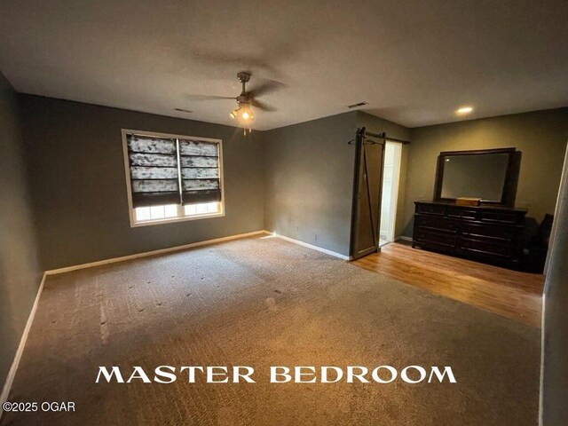 unfurnished bedroom with a barn door, ceiling fan, and carpet