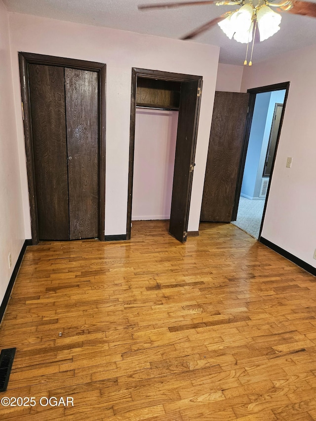 unfurnished bedroom with two closets, light hardwood / wood-style floors, and ceiling fan