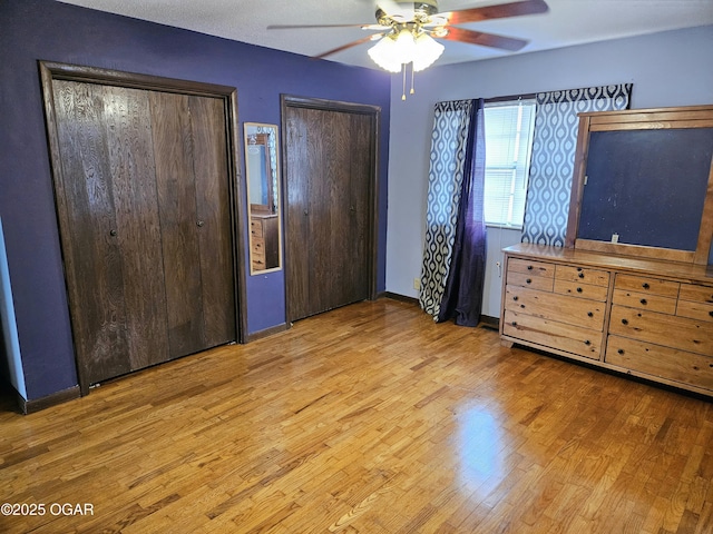 unfurnished bedroom with ceiling fan, wood-type flooring, and multiple closets