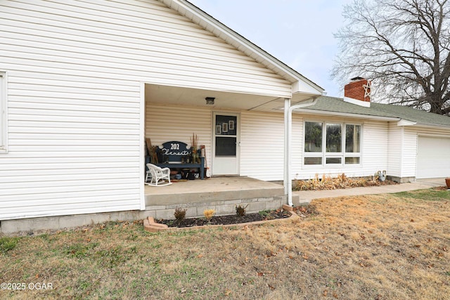 view of exterior entry featuring a lawn, a garage, and covered porch