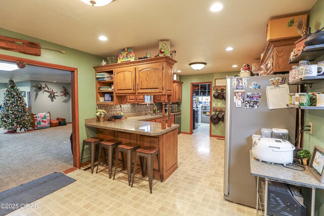 202 Arbor Dr, Lamar, MO 64759 - kitchen with light carpet, separate washer and dryer, a kitchen bar, kitchen peninsula, and stainless steel refrigerator