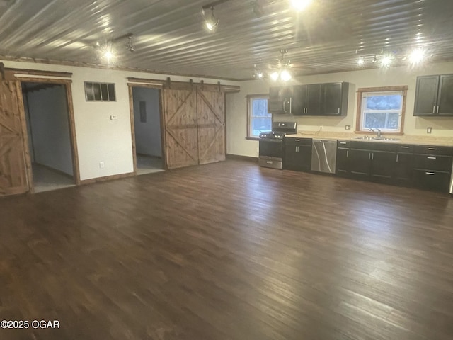 kitchen featuring sink, appliances with stainless steel finishes, ceiling fan, a barn door, and dark wood-type flooring