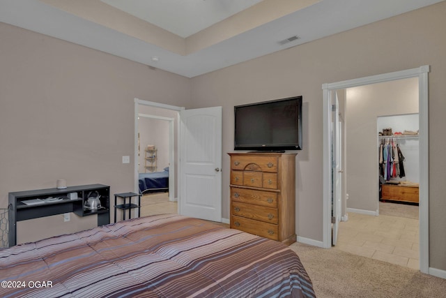 bedroom featuring a raised ceiling, a walk in closet, light carpet, and a closet